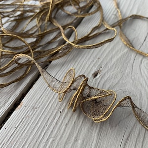 May include: A close-up of gold and black trim, a decorative trim with a metallic gold thread and a black mesh fabric.