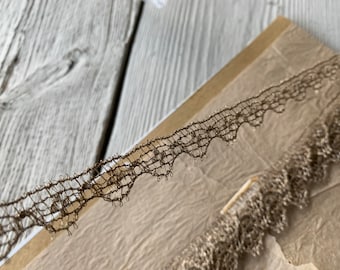 May include: A close-up of a brown metallic lace trim with a scalloped edge. The lace is delicate and has a subtle shimmer.