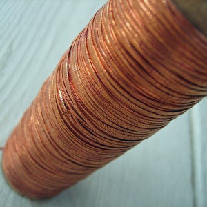 May include: A spool of copper wire, tightly wound and displaying a rich, reddish-brown hue. The wire is neatly arranged, creating a textured surface. The spool is made of wood. This item is suitable for crafting and electrical projects.