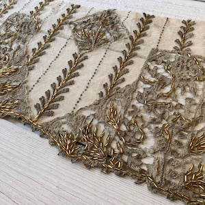 May include: A length of sheer off-white fabric featuring intricate metallic gold embroidery and beadwork. The design consists of repeating vertical vine patterns and rectangular lace panels embellished with gold seed beads and thread.