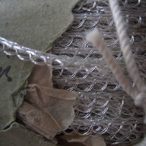 May include: A spool of silver metallic thread with a white string tied around it. The spool is labeled "fine".