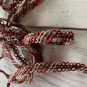 May include: Close-up of decorative trim in a repeating loop pattern. The trim features a combination of red, tan, and brown colors. The trim is likely used for sewing, crafting, or adding embellishments to various projects.