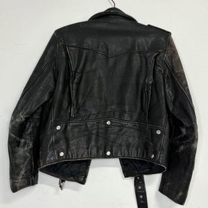 May include: Black leather jacket with silver hardware, hanging on a metal hanger. The jacket has a classic biker style with a notched collar, asymmetrical zipper, and multiple pockets. The leather shows signs of wear.