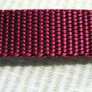May include: Close-up of a deep burgundy woven fabric with a textured, slightly shiny surface.