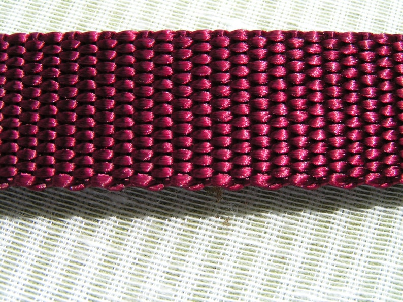 May include: Close-up of a deep burgundy woven fabric with a textured, slightly shiny surface.