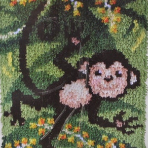 May include: A close-up of a colorful rug with a green, brown, and pink monkey design. The monkey is surrounded by yellow and orange flowers.