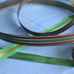 May include: Three different ribbon spools with gold, green and burgundy stripes. The ribbon is a festive and decorative material.