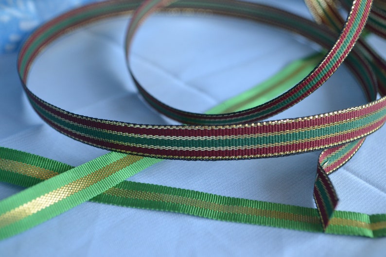 May include: Three different ribbon spools with gold, green and burgundy stripes. The ribbon is a festive and decorative material.