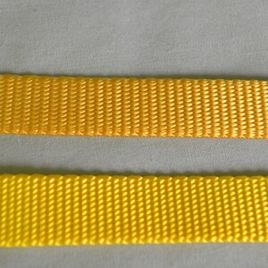May include: Two pieces of yellow webbing, one slightly darker than the other, are shown side-by-side. The webbing is woven with a textured pattern.