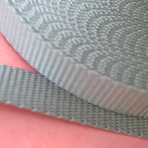 May include: Close-up of a gray woven webbing strap. The strap is made of a durable material and has a textured surface.