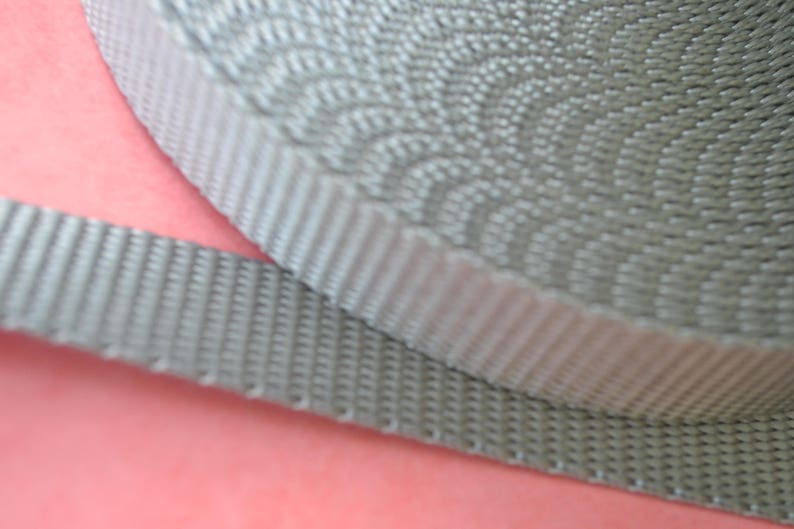 May include: Close-up of a gray woven webbing strap. The strap is made of a durable material and has a textured surface.