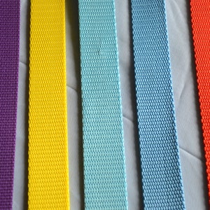 May include: Five different colors of webbing straps. The straps are all the same width and are made of a woven material. The colors are purple, yellow, light blue, blue, and orange.