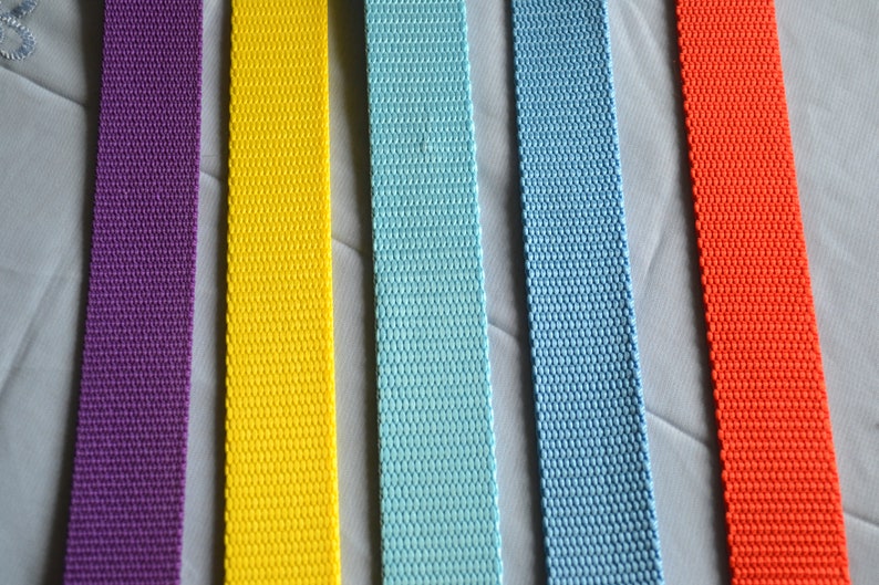 May include: Five different colors of webbing straps. The straps are all the same width and are made of a woven material. The colors are purple, yellow, light blue, blue, and orange.