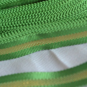 May include: Green ribbon with a gold stripe. The ribbon is rolled up and the gold stripe is visible on the edge.