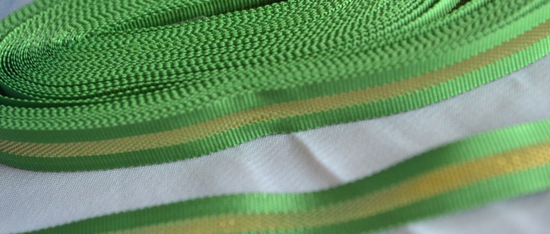 May include: Green ribbon with a gold stripe. The ribbon is rolled up and the gold stripe is visible on the edge.