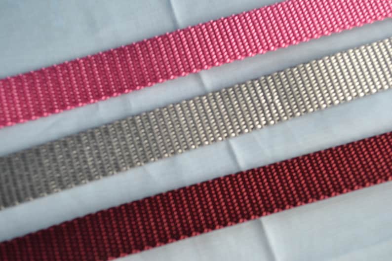 May include: Three different colors of woven webbing, pink, gray, and burgundy.