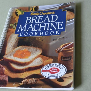 May include: A spiral bound cookbook titled "Betty Crocker's Bread Machine Cookbook" with a photo of bread on the cover. The cover also features a honey jar and a spoon.