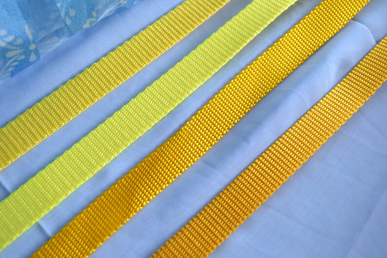 May include: Four different widths of yellow and lime green webbing, laid out on a blue fabric background.