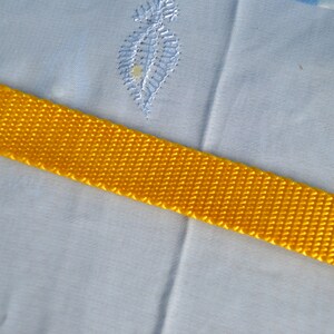 May include: A close-up of a bright yellow woven strap against a light blue fabric background.