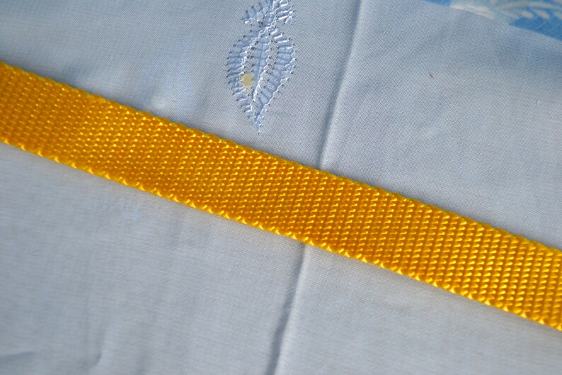 May include: A close-up of a bright yellow woven strap against a light blue fabric background.