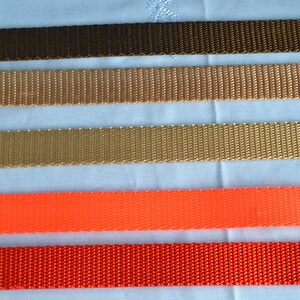 May include: A selection of colorful nylon webbing straps in various shades. The colors include dark brown, tan, gold, orange, and red. The straps are arranged parallel to each other, showcasing their texture and color variations. Ideal for crafting or outdoor gear.