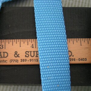 May include: A close-up of a light blue webbing strap, measuring 1 inch wide, against a black surface and a wooden ruler. The ruler has the text "AD & SUP" and a phone number.