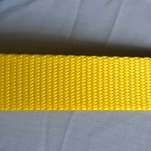 May include: A close-up of a bright yellow woven strap. The strap has a textured surface and is made of a durable material.