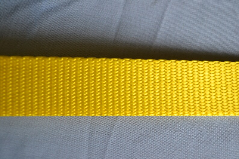 May include: A close-up of a bright yellow woven strap. The strap has a textured surface and is made of a durable material.