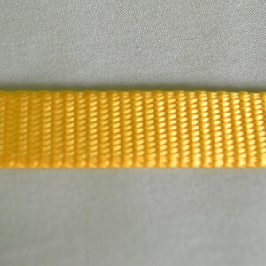 May include: A close-up of a yellow woven strap. The strap is made of a tightly woven fabric with a smooth texture.