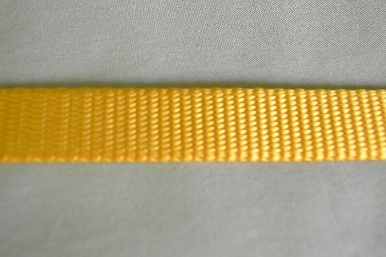 May include: A close-up of a yellow woven strap. The strap is made of a tightly woven fabric with a smooth texture.