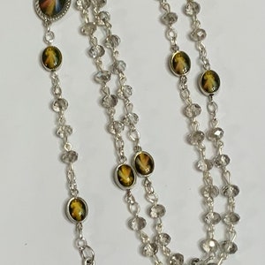 May include: A silver rosary with clear crystal beads and a silver crucifix. The center bead features a picture of Jesus.