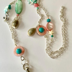 May include: A silver chain with a key ring and a variety of colourful beads, including turquoise, pink, and white. The beads are shaped like seashells, starfish, and fish.