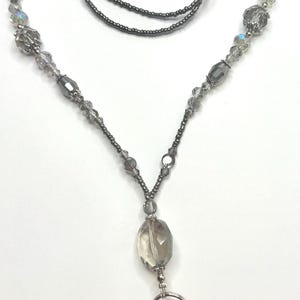 Peut inclure: Un cordon porte-badge perlé gris, orné de perles de différentes formes et tailles. Il est doté d'un fermoir mousqueton et d'un grand pendentif en cristal facetté. Les perles sont enfilées sur un cordon gris foncé.