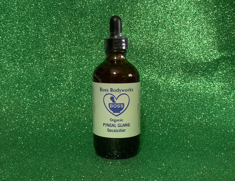 Op de afbeelding: Een bruine glazen fles met een druppelaar, met het label "Boss Bodyworks" en "Organic Pineal Gland Decalcifier". Het label heeft een hart met een vijzel en stamper erin, en het woord "Boss" in blauw.
