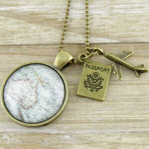 May include: A bronze-coloured necklace with travel-themed charms. The necklace features a round pendant with a map design, a miniature aeroplane, and a passport charm. The passport charm has the word "PASSPORT" and a US seal.