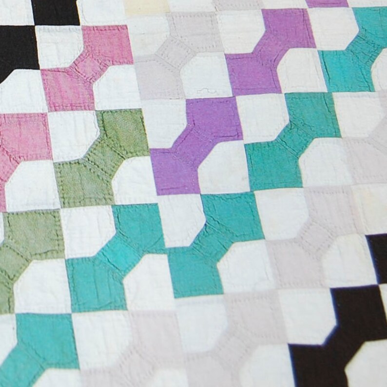 K&ouml;nnte beinhalten: Eine Steppdecke mit einem sich wiederholenden Muster aus wei&szlig;en, schwarzen, rosa, violetten, gr&uuml;nen und t&uuml;rkisfarbenen Quadraten. Die Quadrate sind diagonal angeordnet.