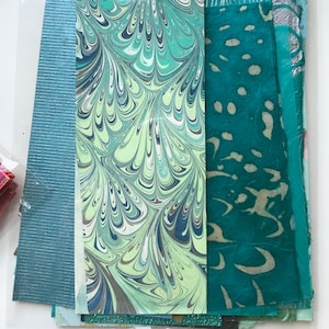 May include: A collection of patterned paper in shades of teal, green, and white. The paper has a marbled, speckled, and textured look.