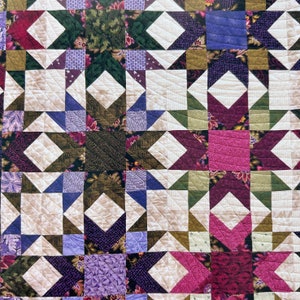May include: A quilt made of various fabrics in shades of green, purple, pink, and white. The quilt is made in a star pattern and is quilted with a white thread.