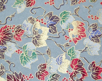 May include: Close-up of a patterned paper with a repeating design of stylized leaves and berries. The leaves are in shades of red, green, blue, and purple, outlined in gold. The background is a muted blue-gray.