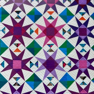 May include: A quilt with a repeating pattern of purple, pink, green, and blue stars on a white background.