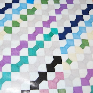 K&ouml;nnte beinhalten: Ein Patchwork-Deckenst&uuml;ck mit einem geometrischen Muster in den Farben Lila, Blau, Gr&uuml;n, Schwarz und Wei&szlig;.