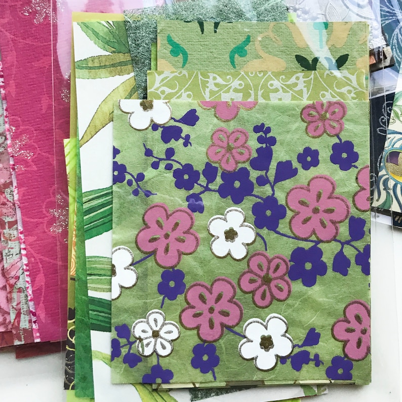 May include: A stack of patterned papers with green, pink, white, and purple floral designs. The papers are arranged in a vertical stack, with the top paper featuring a green background with pink and white flowers.