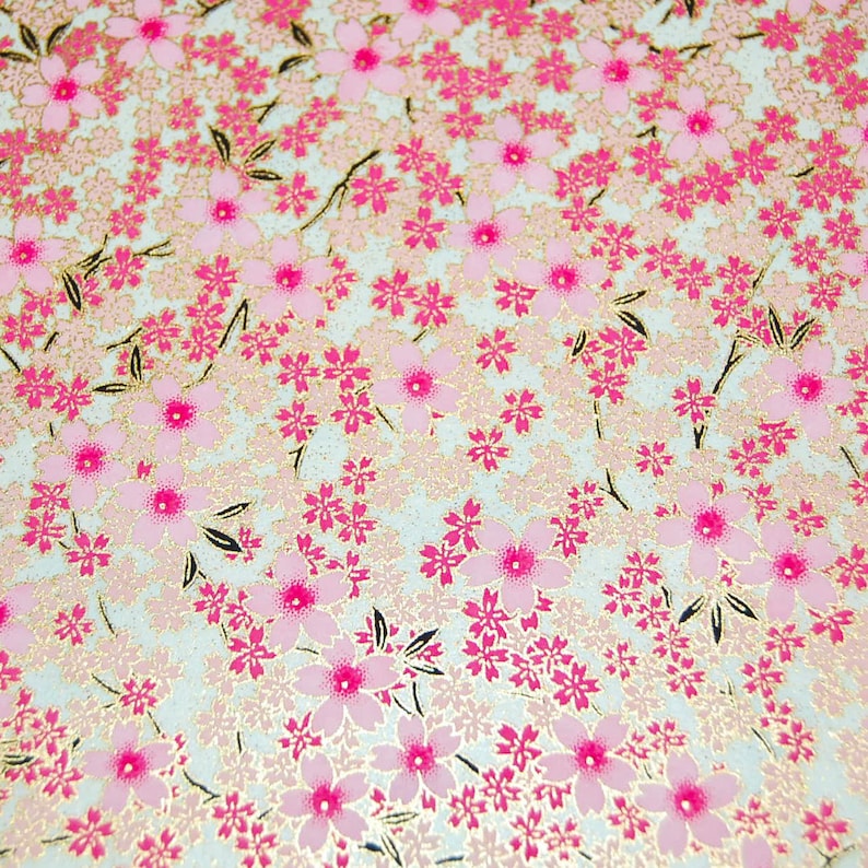 May include: A white background with a pink and gold floral pattern. The pattern is made up of small pink flowers with gold centers and gold leaves.