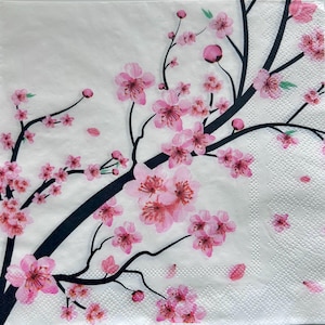 May include: A white paper napkin with a pink and black floral design. The design features a branch of cherry blossoms with pink flowers and black stems.