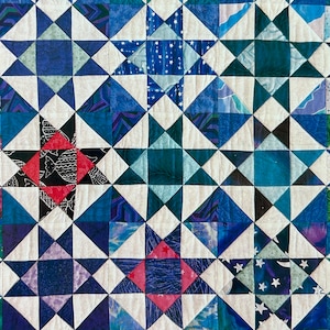 May include: A quilt made of blue, white, and red fabric with a star pattern. The quilt is made up of many smaller squares, each with a different pattern.