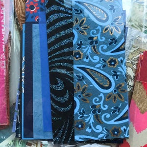 May include: Assortment of patterned paper scraps in blue, black, gold, and white. The paper scraps feature paisley, floral, and geometric designs.