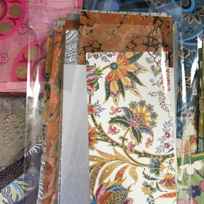 May include: A stack of patterned papers with a floral design in shades of blue, red, yellow, and green. The papers are layered on top of each other and have a variety of textures.