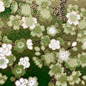May include: Close-up of a decorative paper with a floral pattern. The design features white, light green, and dark green flowers with gold accents on a dark green background. The flowers are clustered together.