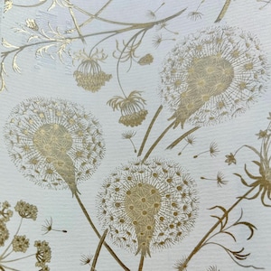 May include: Close-up of a white background with a gold dandelion pattern. The design features detailed illustrations of dandelion seed heads, stems, and other floral elements. The gold color provides a luxurious and elegant feel to the design.