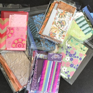 May include: Assortment of colorful patterned paper scraps in clear plastic bags. The papers feature floral, geometric, and abstract designs.